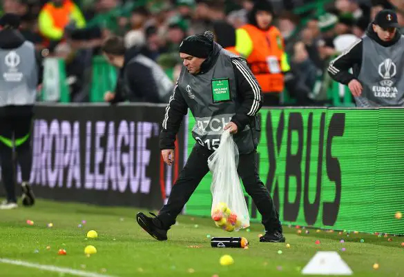 A Celtic steward picks up tennis balls after fans threw them onto the pitch in protest at the beginning of last night's Europa League fixture.